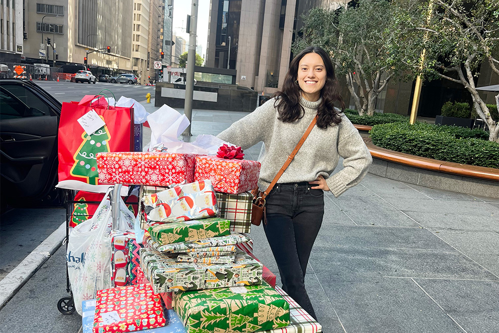 An ARA employee standing in front of a stack of donated wrapped gifts